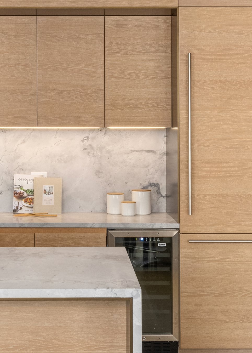 A closeup of the kitchen island with flowers sitting on it, part of a stool in the foreground and cupboards, a cooking surface and backsplash behind it.